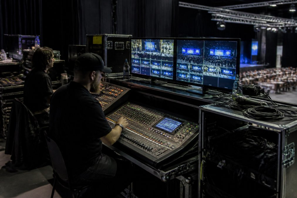 Professional live streaming control room with multiple monitors displaying video feeds, audio mixing console, and technicians managing broadcast operations