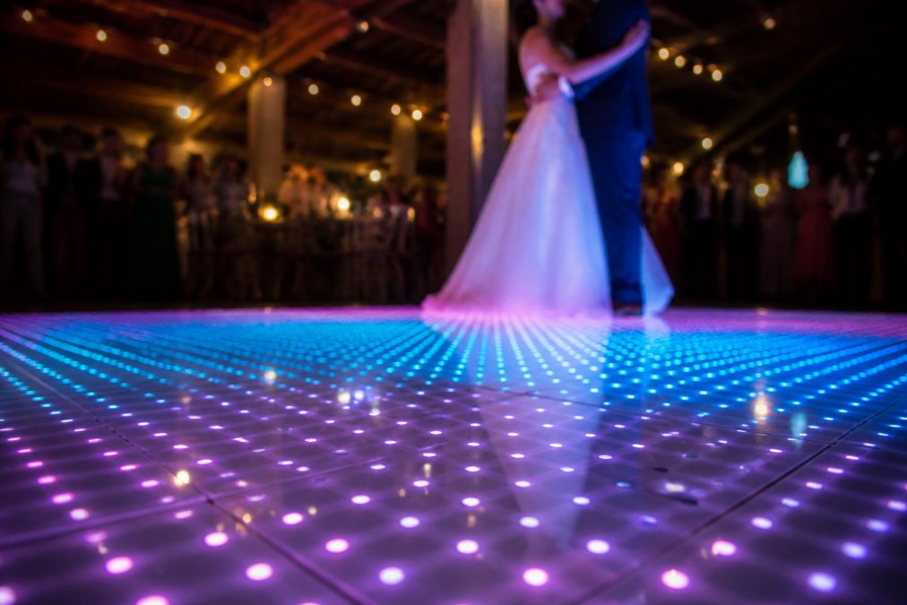 Close-up van LED-pixels op een verlichte dansvloer met kleurrijke blauwe en paarse effecten, terwijl een bruidspaar in de achtergrond danst en de pixeldetails duidelijk zichtbaar zijn