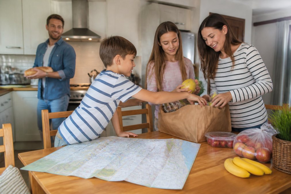 Family unpacking groceries in a budget holiday rental kitchen with a map of local Hemel Hempstead attractions.