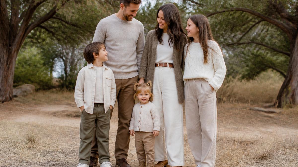 Family of four wearing coordinated neutral layered outfits in soft natural light