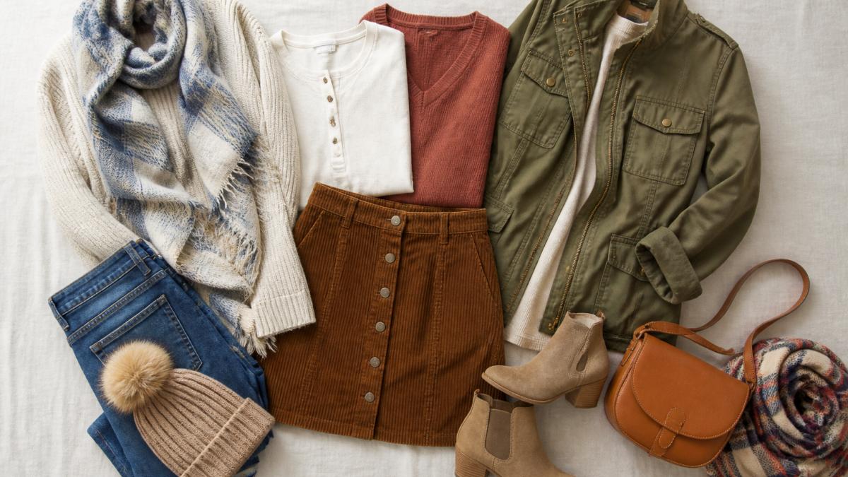 Flat lay of coordinating neutral and accent clothing pieces arranged on a light surface showing how seasonal capsule pieces work together, including a corduroy skirt, layering pieces, a lightweight jacket, and accessories in coordinating tones