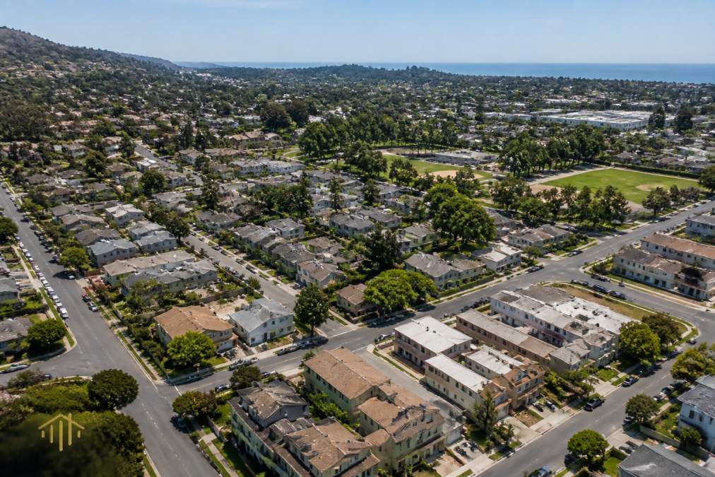 Aerial view of a residential neighborhood with a mix of single-family homes and multi-unit properties, tree-lined streets, and community parks visible below