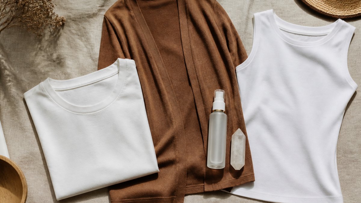 Flat-lay of a neutral-toned clothing set, skincare bottle, and meditation crystal on linen fabric.