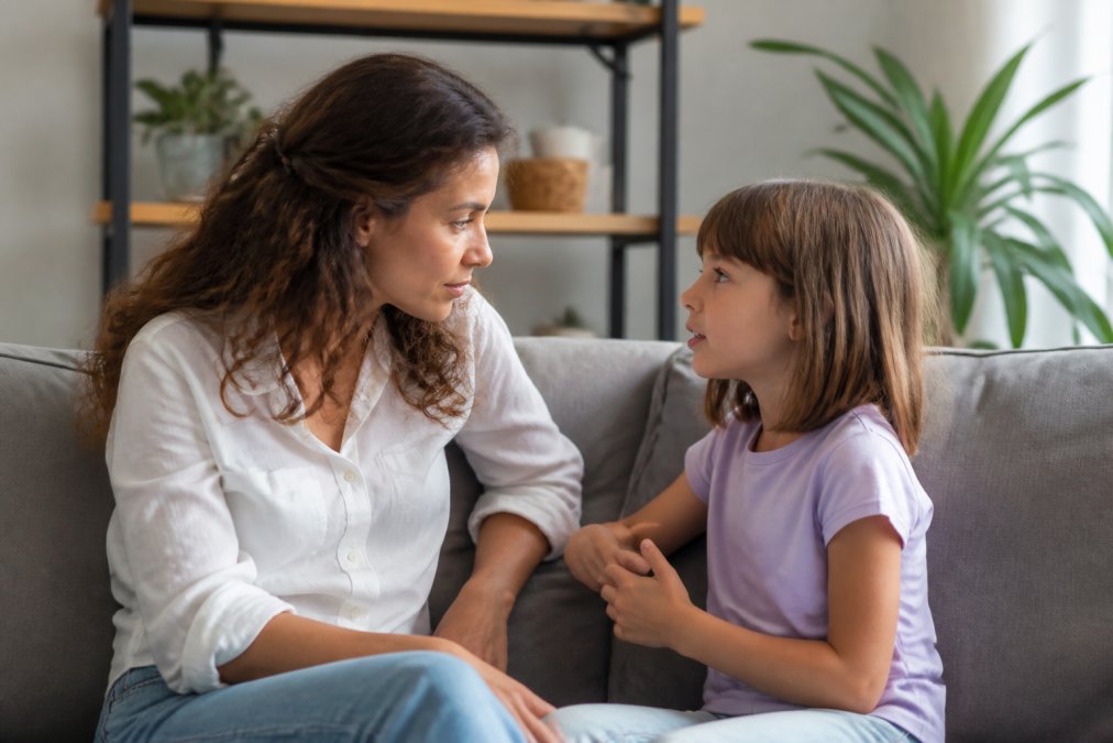 Parent and young child sitting together on a couch, parent listening attentively as child speaks, warm home setting with soft lighting