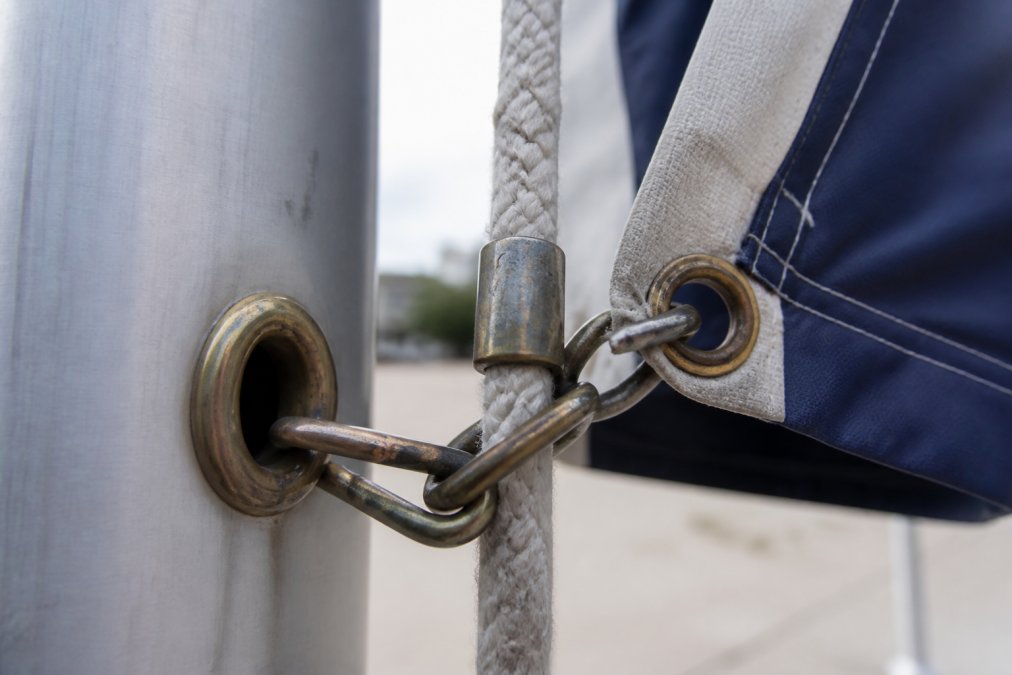 Close-up of weathered brass grommets and metal snap hooks on a commercial flagpole halyard system, showing wear patterns and material durability