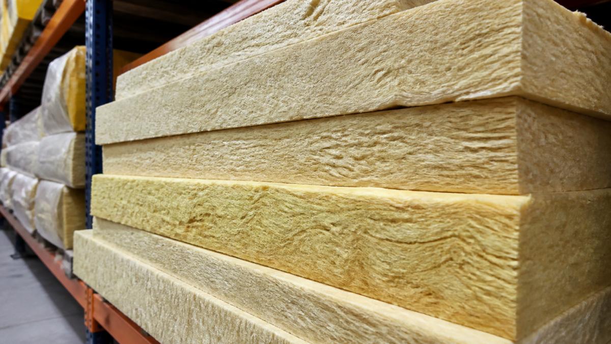 Close-up of stacked insulation batts showing various thicknesses and fibreglass material density in a warehouse storage bay with industrial shelving