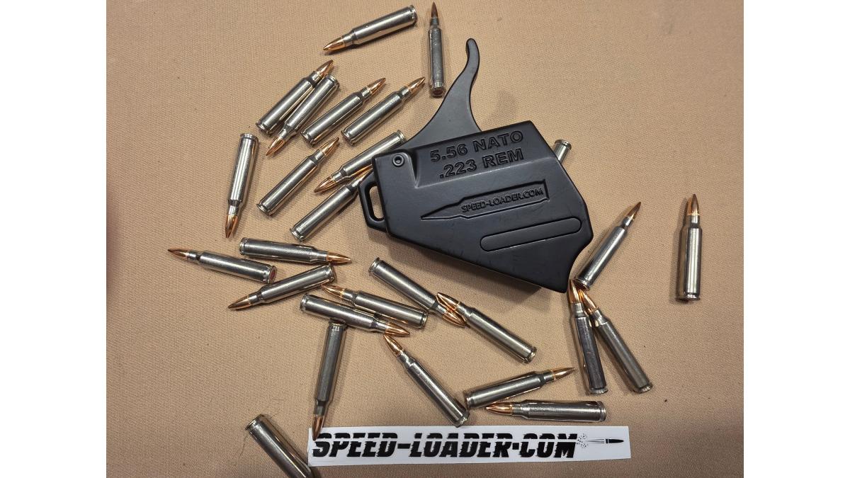 Close-up of hands using a black polymer magazine speed loader to press rounds into an AR-15 magazine on a wooden shooting range bench, late afternoon sunlight