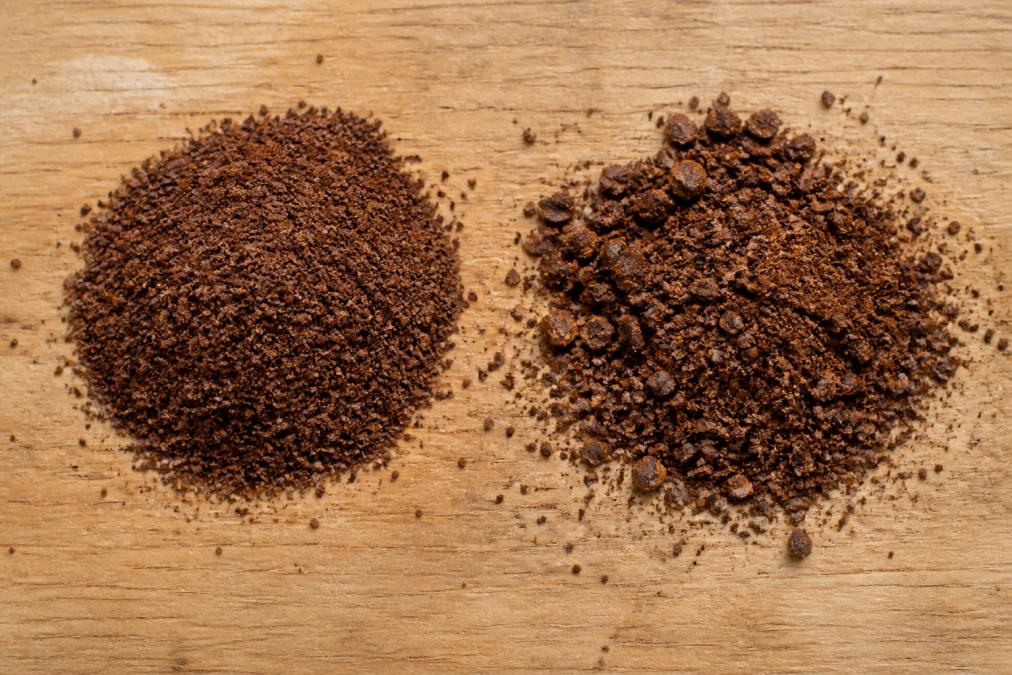 Uniformly ground coffee next to a pile with inconsistent particle sizes on a wooden table.