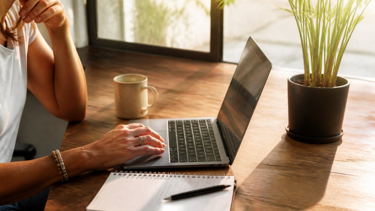 A consultant sitting at a tidy home-office desk reviewing program options on a laptop, notebook and coffee beside the keyboard, soft morning light through a window