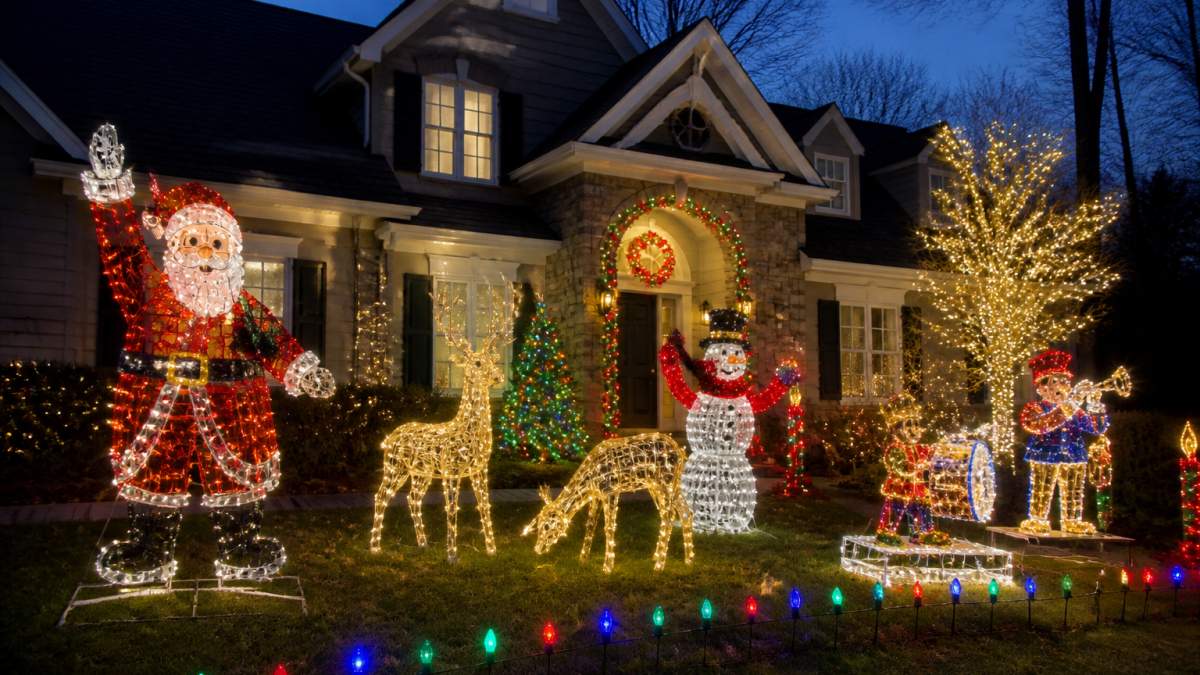 Professional residential home at dusk displaying multiple animated Christmas light sculptures across the front yard, including illuminated Santa figures with side-to-side motion, glowing reindeer, and musical light-up scenes creating a festive holiday atmosphere