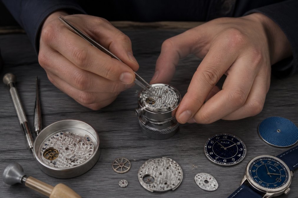 Watchmaker's hands assembling intricate mechanical movement components with precision tweezers and specialized tools on a well-lit workbench, showing caliber assembly and bridge finishing