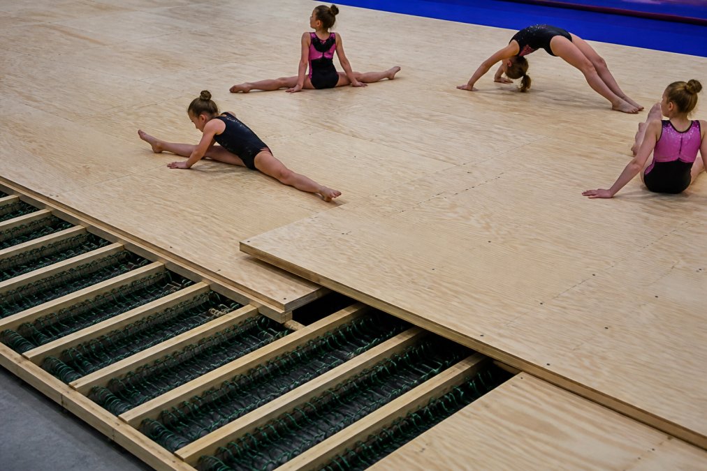 Overhead view of a professional Baltic birch spring floor in a gymnastics facility with athletes training on the surface, showing the two-layer construction and spring system in action