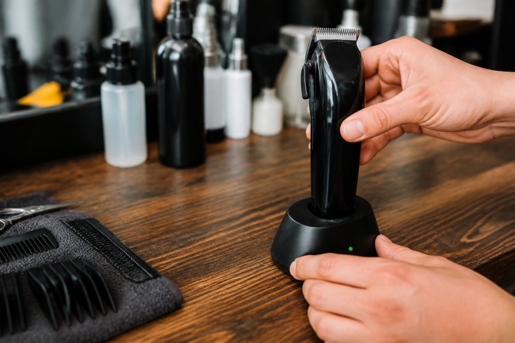Close-up of hands properly placing a cordless clipper on a charging dock with LED indicator lights visible, demonstrating correct charging technique