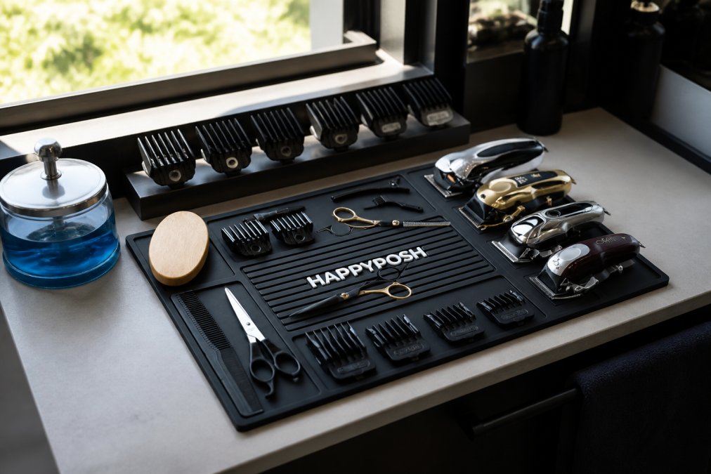 Professional barber station with magnetic mat holding organized clippers, guards neatly arranged in a holder, and disinfectant jar positioned at station corner, natural daylight from window illuminating the workspace