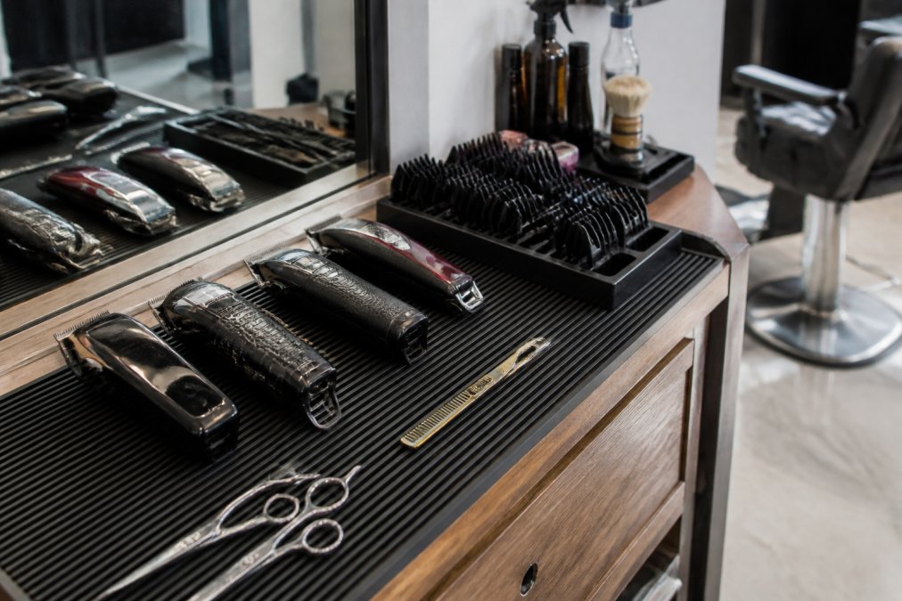 Professional barber station with organized clippers, guards, and tools neatly arranged on a magnetic mat with a guard holder visible, showing a clean, well-lit workspace ready for service