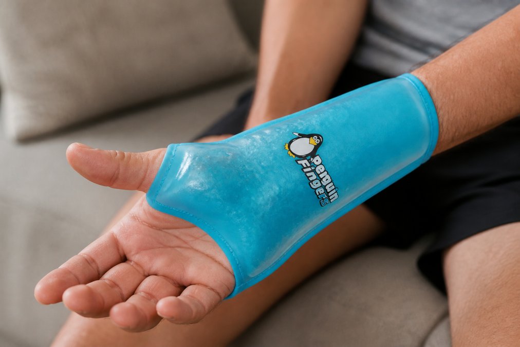 Close-up of a person's wrist and hand wearing a translucent blue gel-filled compression sleeve, showing the flexible material conforming to the skin with visible gel pack detail and the sleeve's slip-on design