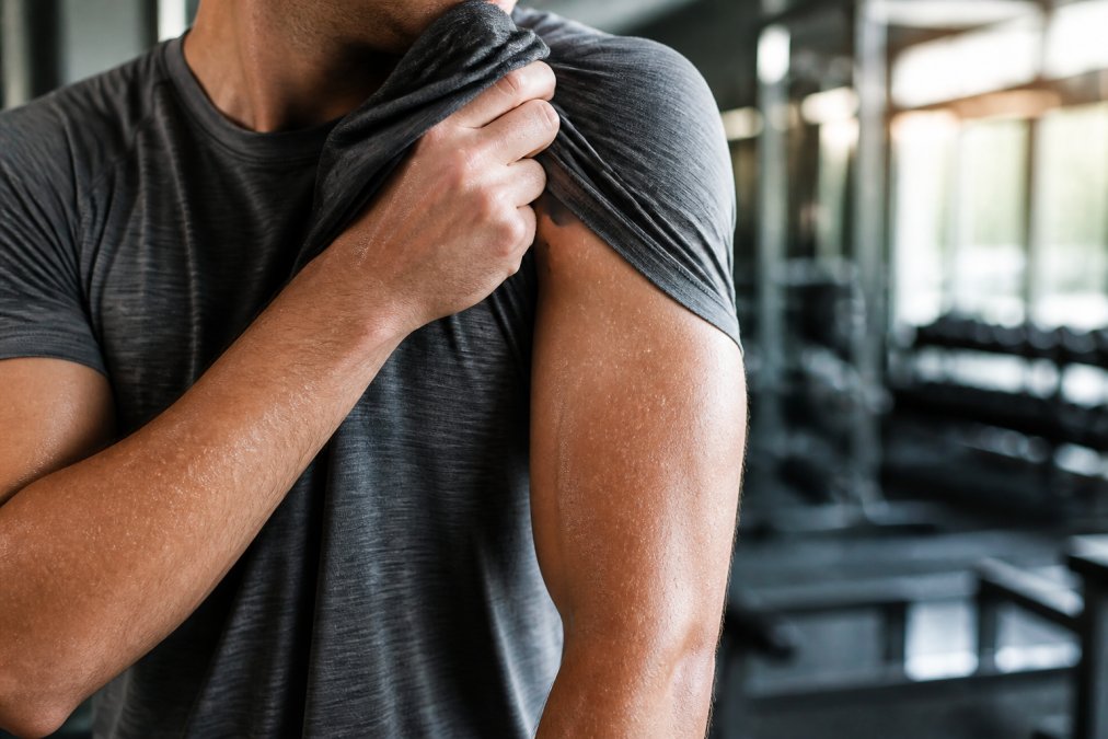 Athlete wiping sweat with moisture-wicking comfortable training apparel that repels droplets in a sunny gym