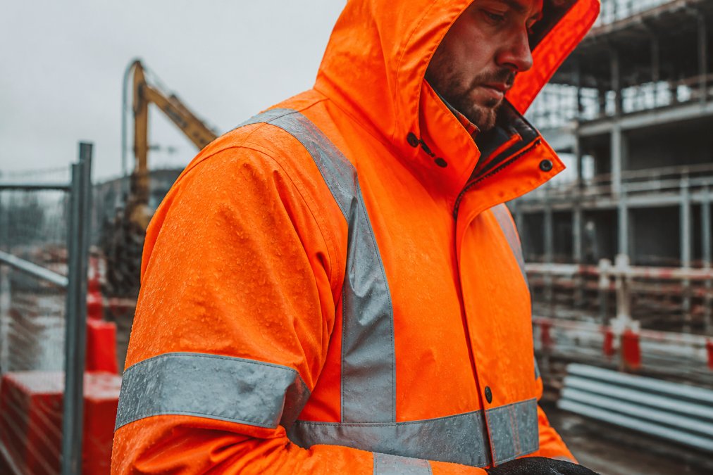 Worker in a waterproof hi vis jacket with reflective tape as rain beads on the fabric at a construction site