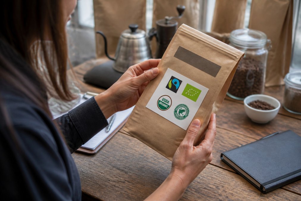 Close-up of hands holding a coffee bag, examining certifications and labels on the packaging in natural light