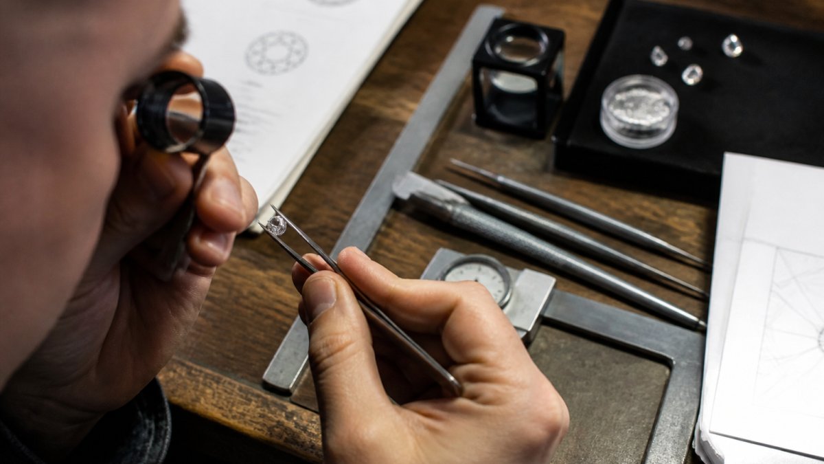 Jeweler examining a loose diamond under magnification with certification documents at a workbench