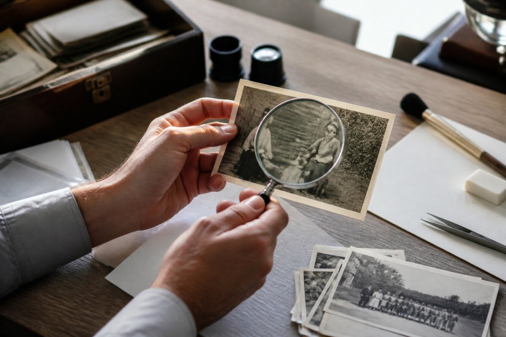 Collector examining the paper texture of historical photographs with a magnifying glass