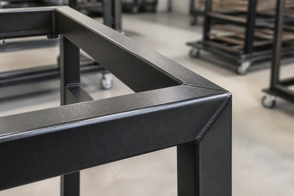 Close-up of a powder-coated heavy duty steel furniture frame featuring precision mitered welds in a workshop.
