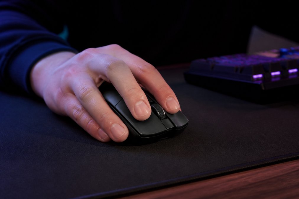 Close-up of a hand gripping a lightweight, modern wireless gaming mouse on a dark RGB-lit gaming mousepad in a dimly lit room