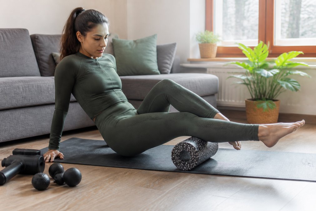 Person using foam roller on legs while wearing compression activewear in home setting, demonstrating combined recovery routine with natural window lighting