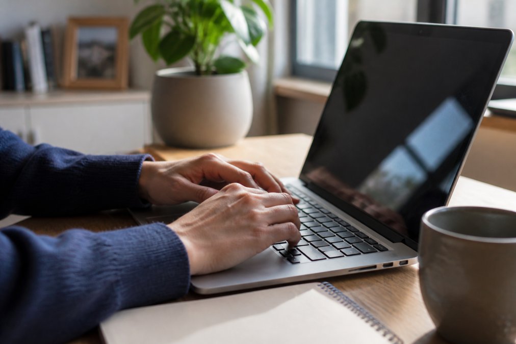 Close-up of hands typing payment details on a laptop in a warm home office, with a small padlock icon visible in the browser address bar and a coffee mug nearby