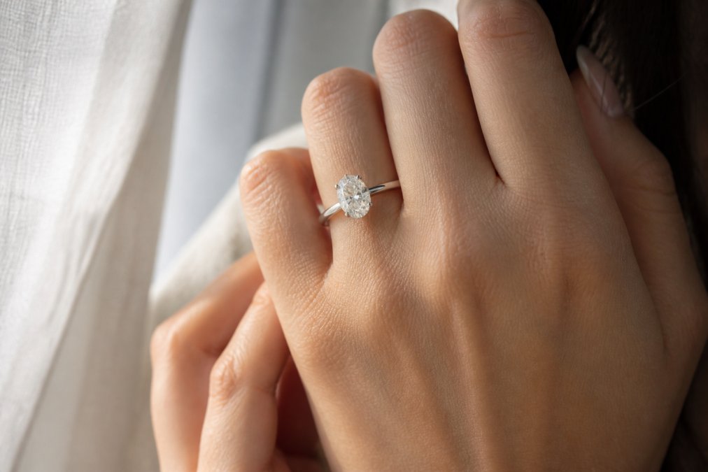 Close-up of a woman's hand wearing a sparkling oval cut lab grown diamond engagement ring in 14K white gold, soft natural window light creating gentle reflections on the stone