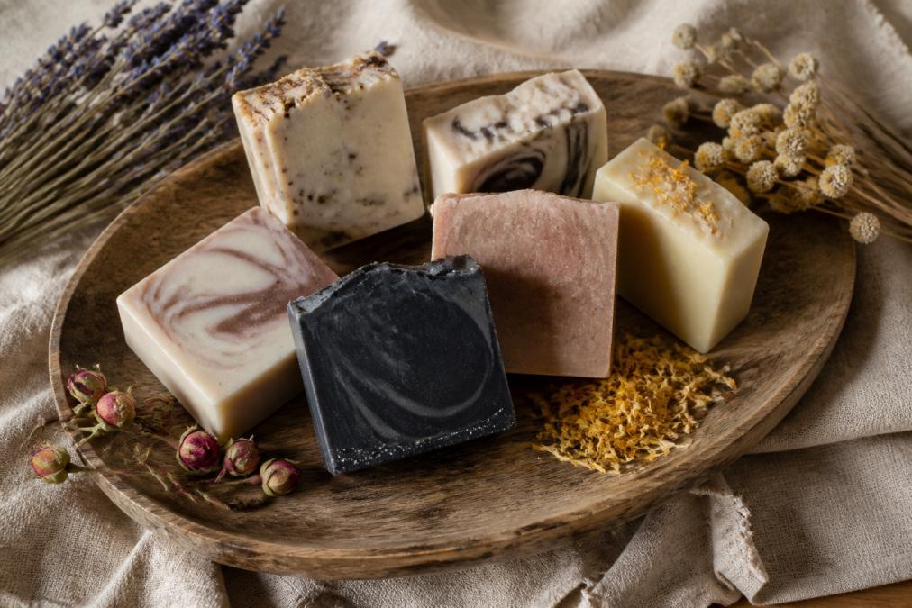 A collection of handcrafted soap bars arranged on a rustic wooden tray with dried botanicals and a linen cloth, soft natural lighting highlighting the marbled textures and natural colors of each bar