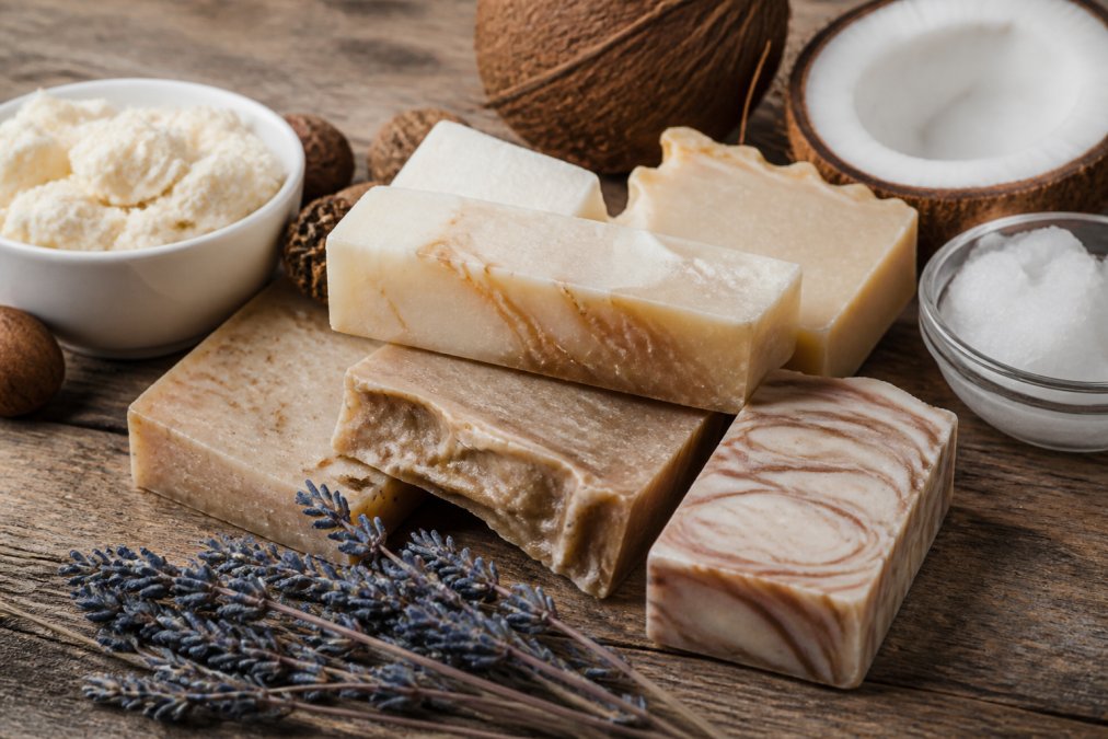 Natural handmade soap bars arranged on wood with lavender, shea butter pods, and coconut oil under soft lighting.