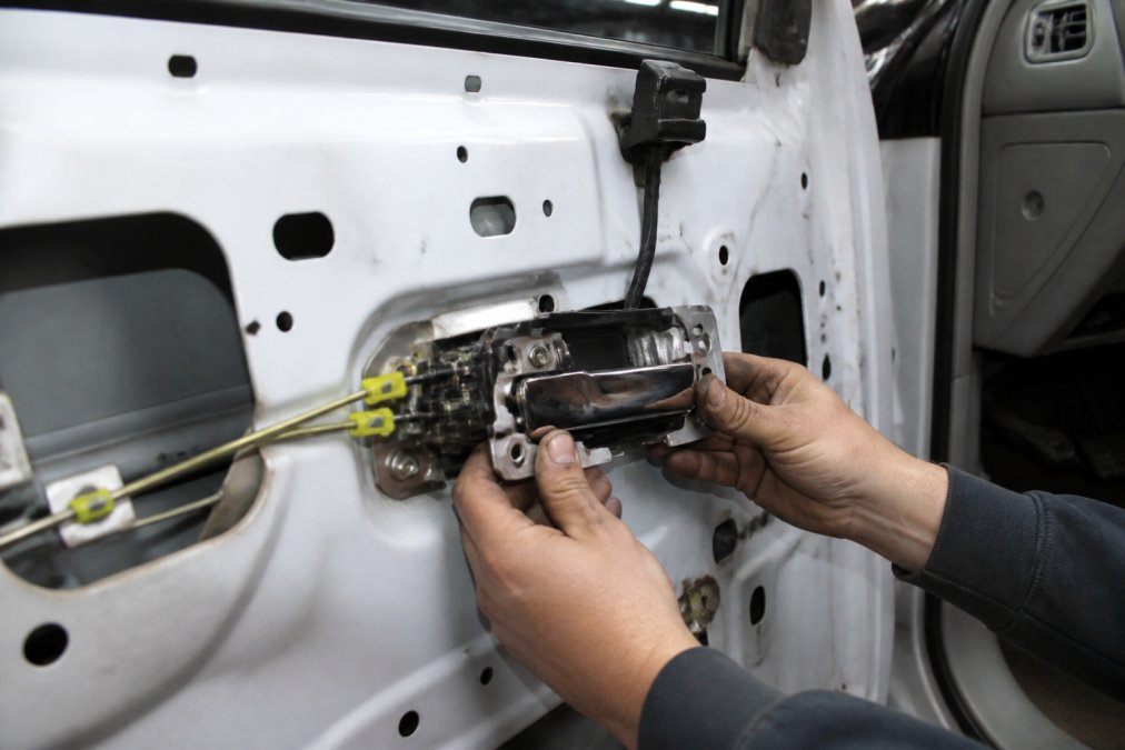 Mechanic's hands installing a billet door handle assembly into an OBS Chevy truck interior, showing the direct fit connection to the door lock mechanism and the mechanical rod linkage with professional workshop lighting