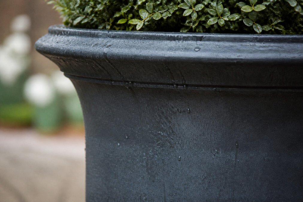 Close-up detail of weathered glazed ceramic outdoor urn showing subtle patina and texture, with water droplets catching light on the surface, displaying natural aging and character
