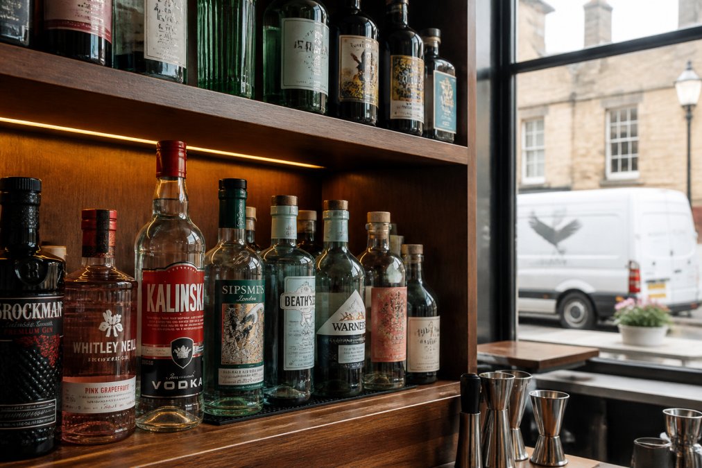 Well-stocked bar shelves displaying premium spirit bottles alongside craft spirits, with a white van visible through the window outside a traditional gastropub