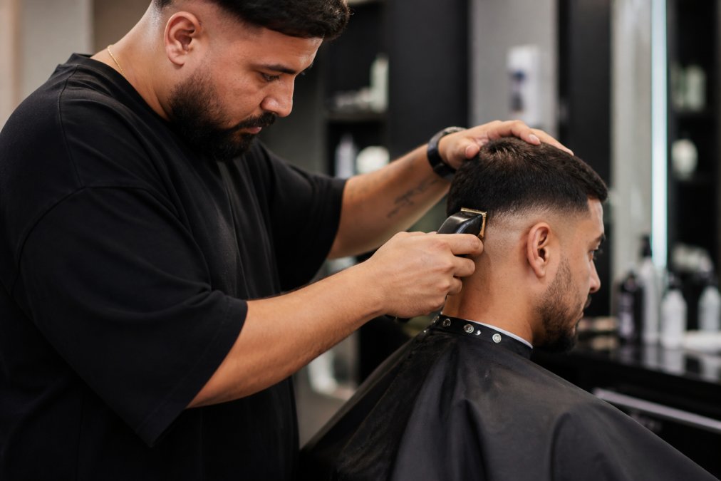 Professional barber using a high-performance cordless clipper on a client's fade, demonstrating precise cutting technique with proper ergonomic grip and focused concentration