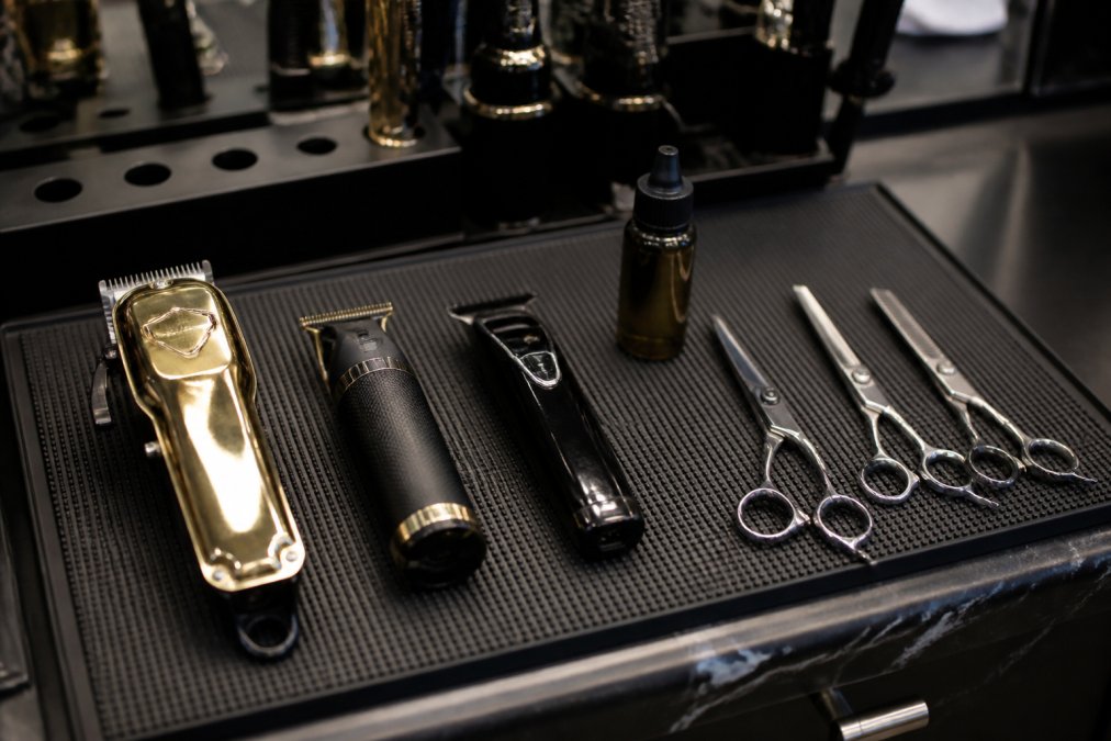 Close-up of a professional barber station countertop with cordless clippers, a trimmer, shears, and blade oil arranged neatly on a dark magnetic mat