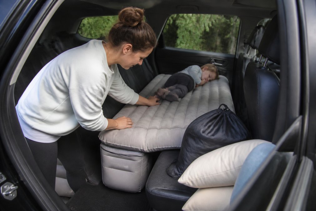 Caregiver adjusting an inflatable travel bed in an SUV backseat while a toddler rests nearby