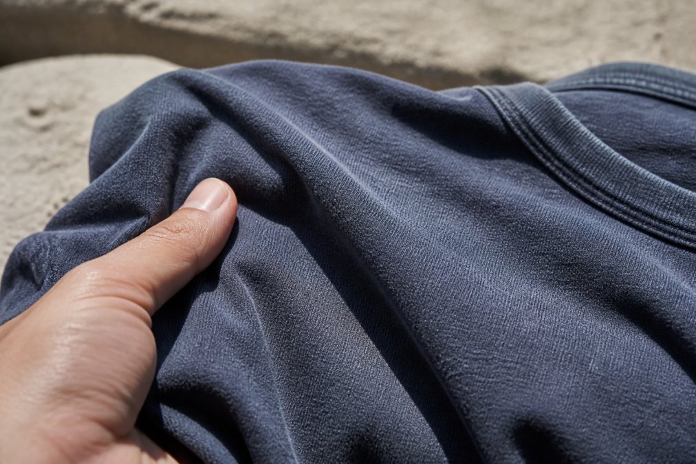 Close-up of a person's hand holding the fabric of a faded navy graphic t-shirt, showing the soft colour and texture in natural outdoor light