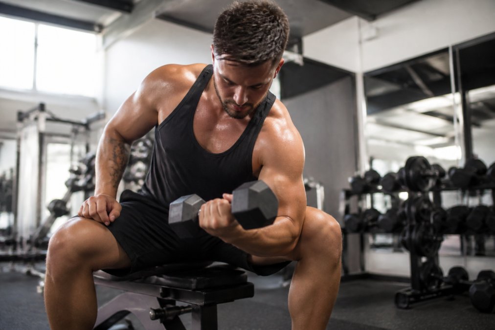 Person lifting a dumbbell in a gym wearing black sweat resistant shorts and a singlet