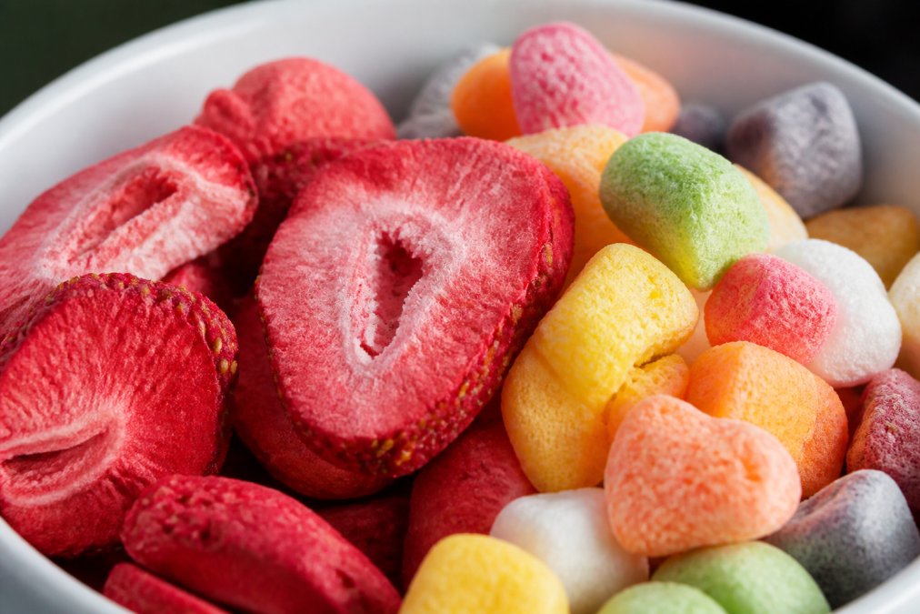 Close-up of vibrant freeze-dried strawberry pieces and mixed fruit candy with visible airy, puffed texture under bright natural light, showing the concentrated color and delicate structure