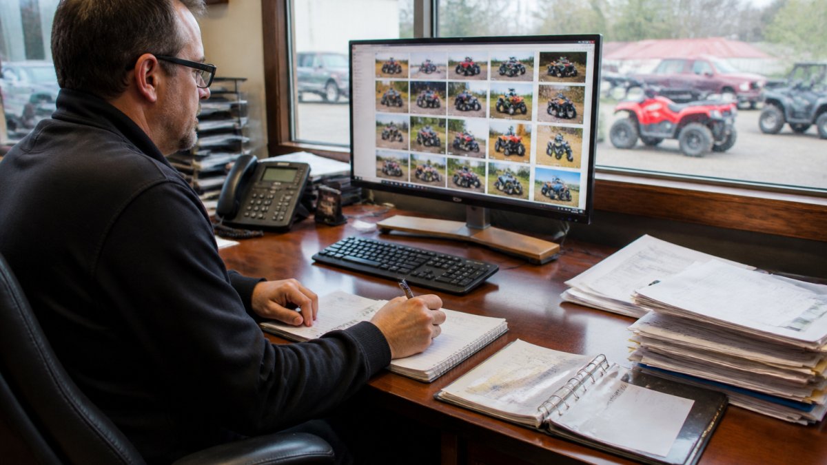 Professional at desk reviewing supplier documentation and credentials on computer screen, with notebook and pen for notes, natural office lighting