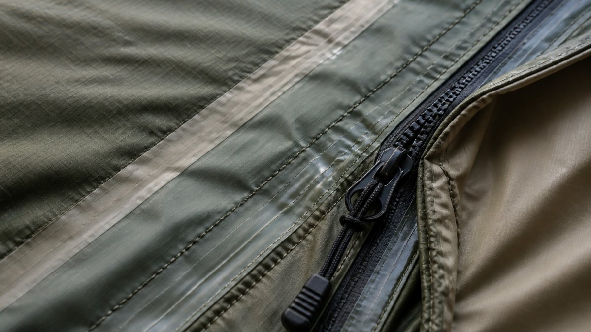Close-up of tent seam with waterproof tape, showing zipper mechanism and ripstop nylon fabric texture under natural lighting