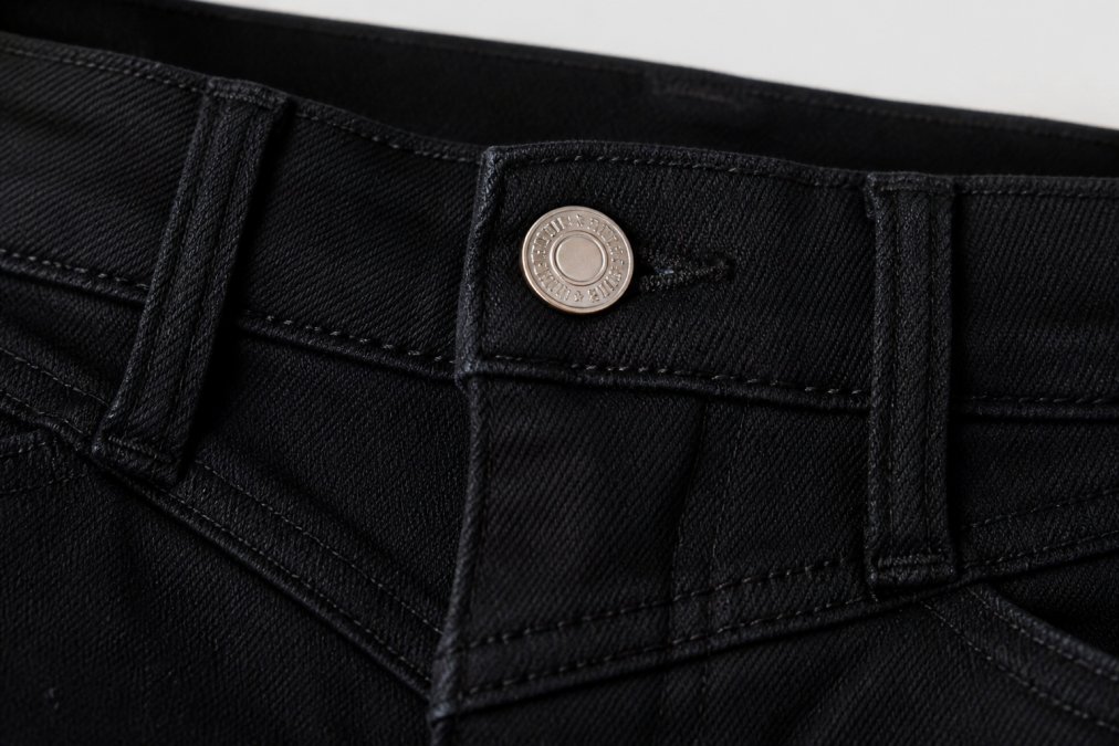 Detailed close-up of high-quality stitching on a denim garment, showing tight, even seams and reinforced button attachment with multiple rows of stitching