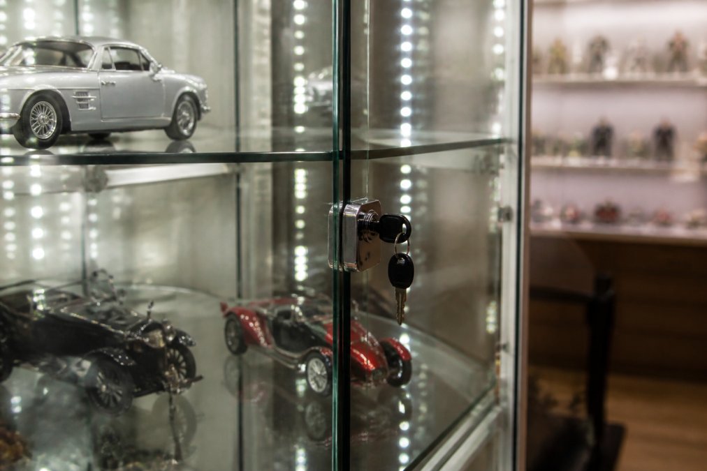 Close-up of a lockable glass display cabinet with visible hinged door and secure locking mechanism, displaying collectible items inside with LED lighting illuminating the contents