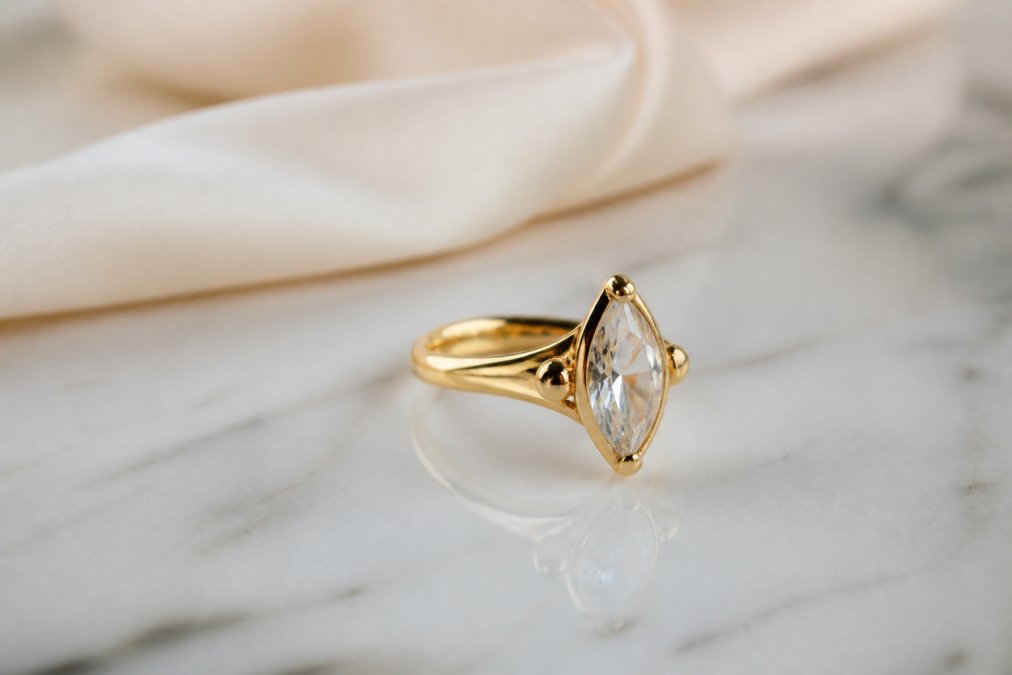 Close-up of an 18k yellow gold cocktail ring set with an antique marquise diamond, resting on a smooth marble surface with soft natural light highlighting the stone's facets