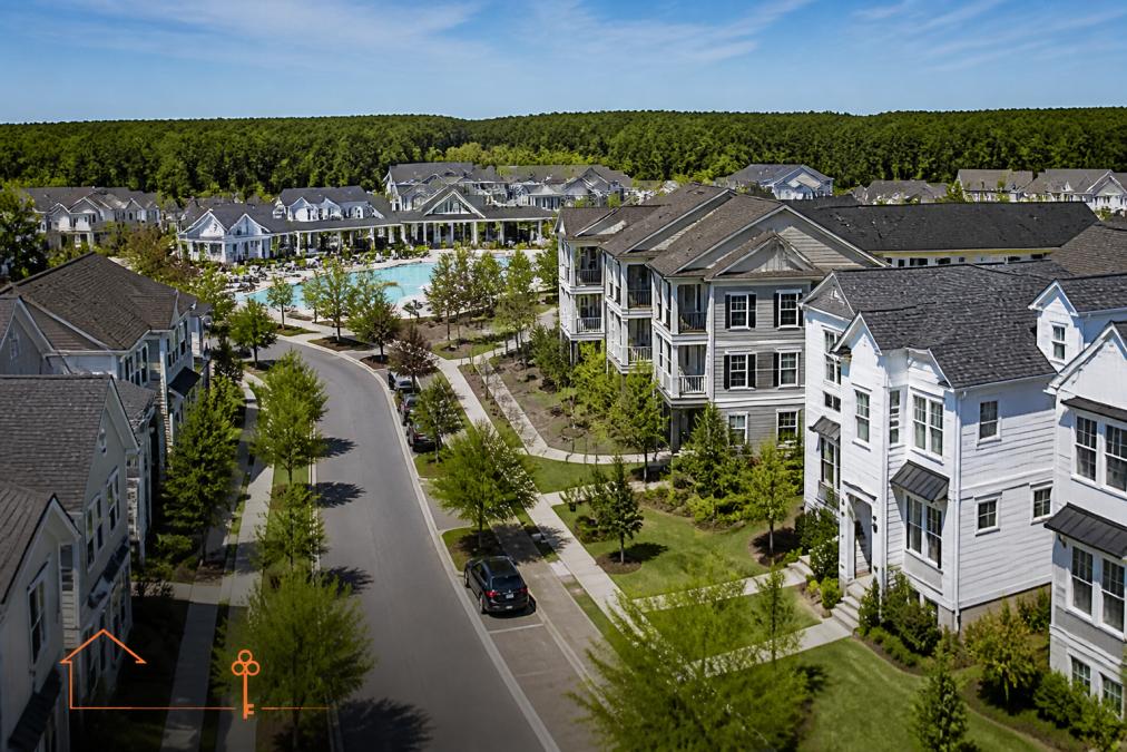 Aerial view of a modern master-planned community with tree-lined streets, new townhomes and single-family homes with manicured landscaping, community center and pool visible in background