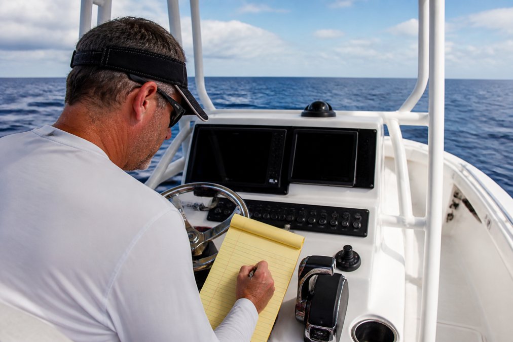 Boat owner calculating amp hour requirements on a notepad at the helm of a center console fishing boat