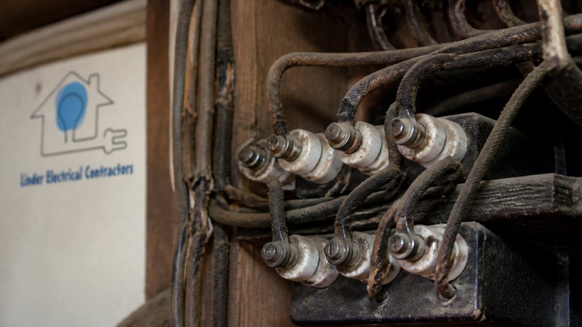 Close-up of vintage knob-and-tube wiring inside an older home electrical panel, showing deteriorated insulation and ceramic insulators mounted on wooden framing