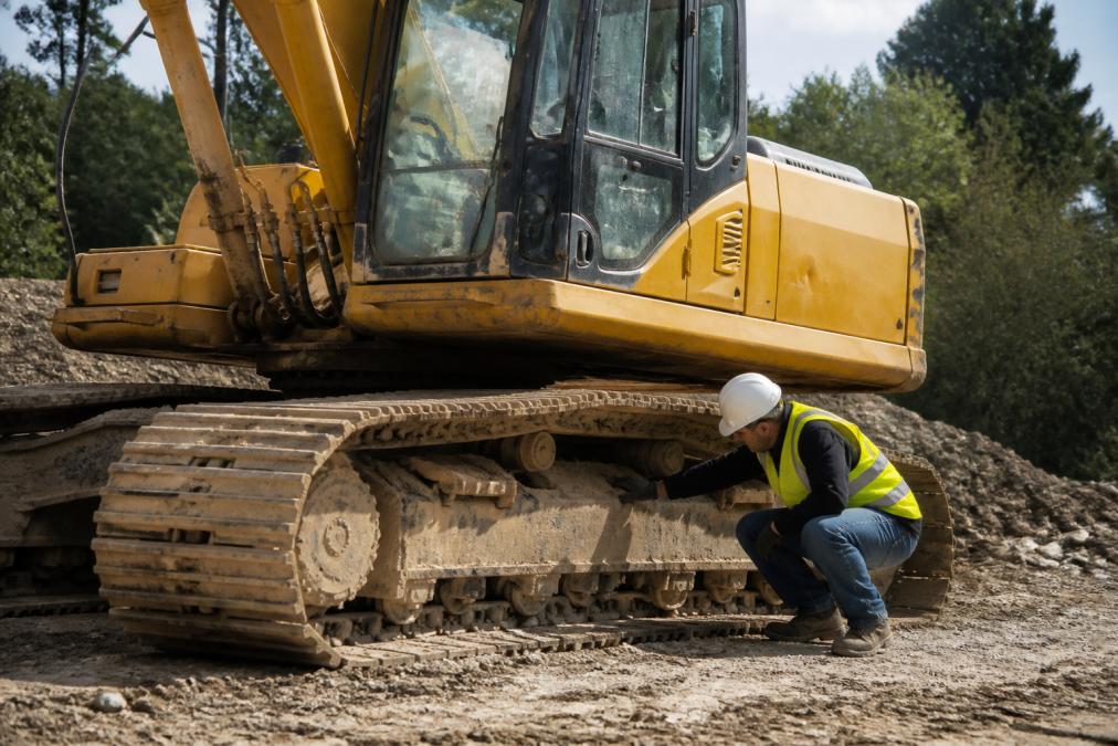 A well-maintained older excavator on a construction site with an operator inspecting the undercarriage in daylight